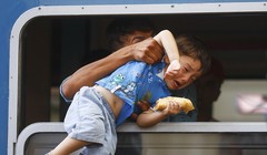 Một chú bé đang được cố kéo qua cửa sổ để lên con tàu chật ních những người chạy nạn đói khát và tuyệt vọng