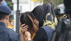 Nghi phạm Đoàn Thị Hương (áo vàng) che mặt khi bị cảnh sát áp giải tới phiên tòa. (Ảnh: AFP)