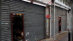 Chủ một cửa hiệu quan sát cuộc biểu tình qua cánh cửa đóng kín tại Sheung Shui (Ảnh: Reuters)