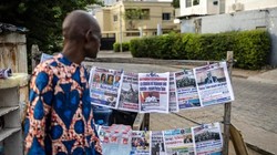 Một người bán hàng đang xem những tờ báo được trưng bày trên một gian hàng ở Cotonou, vào ngày 8/12. Ảnh: AFP.