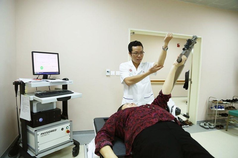Bác sĩ hướng dẫn bệnh nhân tập phục hồi chức năng với máy.