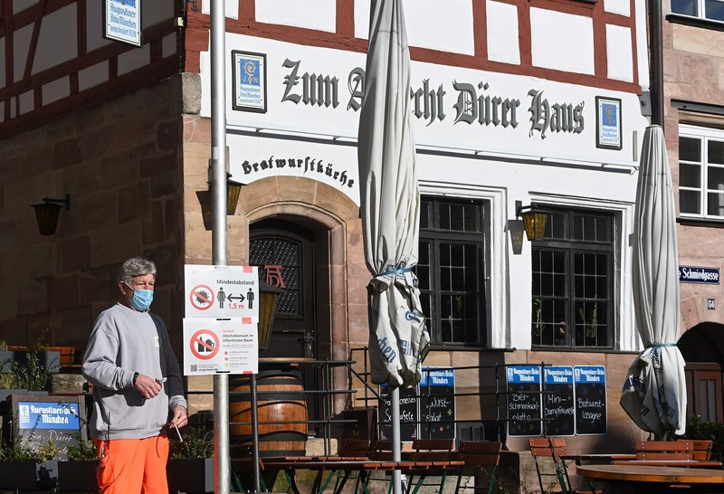 Một người dân đứng cạnh tấm biển hướng dẫn phòng chống COVID-19 ở Nuremberg, Đức (Ảnh: NBC)