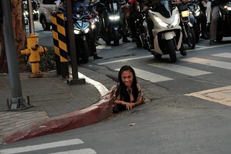 Một người phụ nữ được chụp ảnh đang chui ra khỏi một lỗ thoát nước dọc theo một con phố ở thành phố Makati, Philippines. Ảnh: William Roberts.