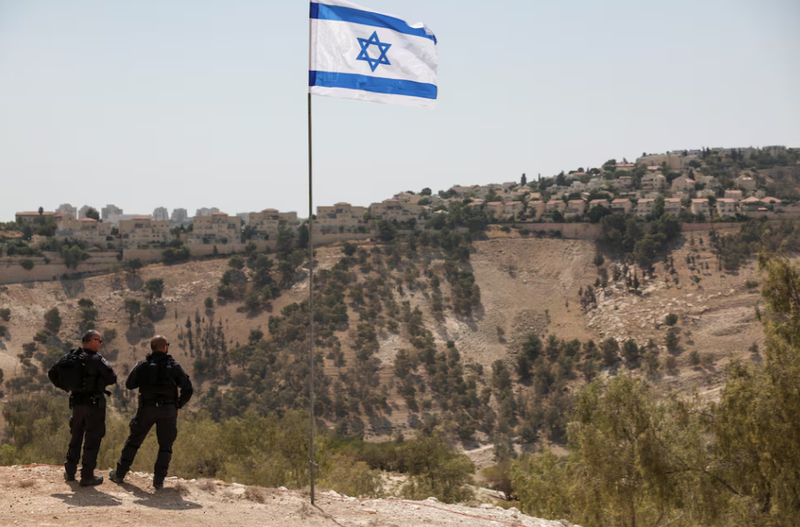 Lá cờ Israel tung bay, một phần của khu định cư Maale Adumim của Israel có thể được nhìn thấy ở phía sau, tại khu Bờ Tây do Israel chiếm đóng, ngày 14/8. Ảnh: Reuters.