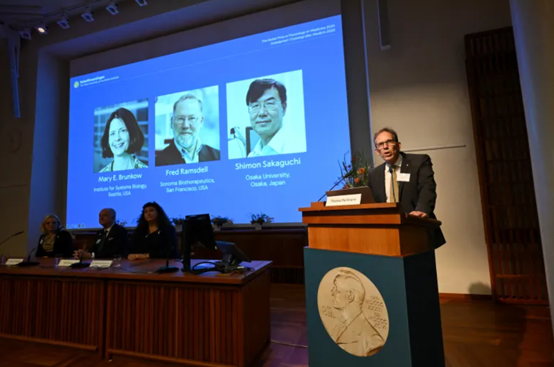 Tổng thư ký Ủy ban Nobel Thomas Perlmann phát biểu trước màn hình hiển thị chân dung các nhà khoa học đoạt giải tại Viện Karolinska ở Stockholm, Thụy Điển. Ảnh: AFP. Phát hiện vệ sĩ tàng hình của hệ miễn dịch, ba nhà khoa học nhận giải Nobel Y học 2025.png