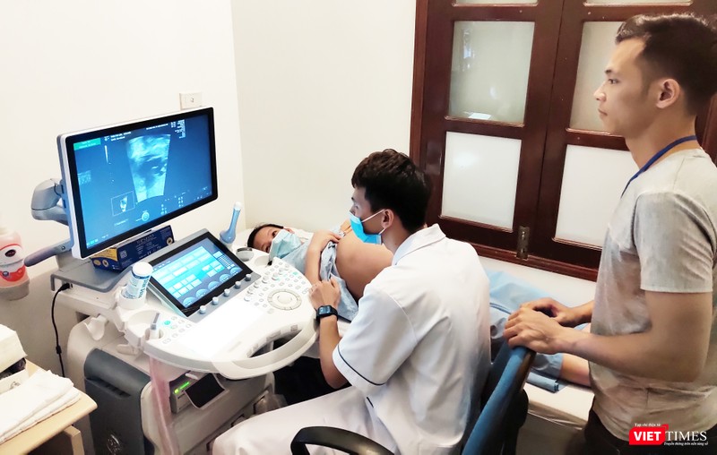 Bác sĩ tiến hành nội soi cho chị Liên (áo xanh đeo khẩu trang), chồng chị Liên anh Triệu Văn Sơn (áo xám) đứng cạnh dõi theo hình ảnh của 2 bé gái. Ảnh: Minh Thúy