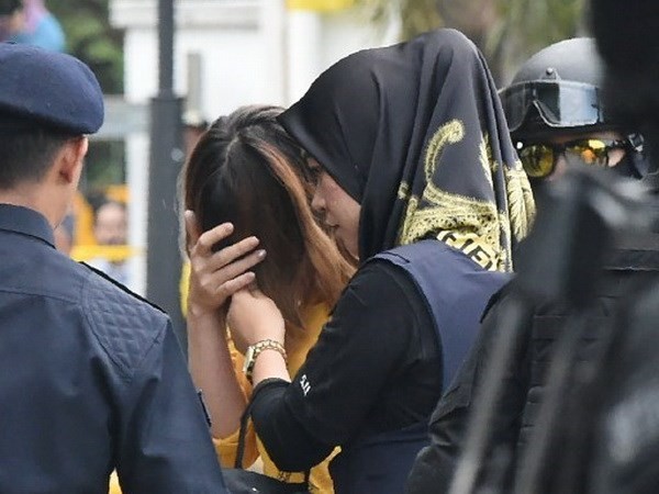 Nghi phạm Đoàn Thị Hương (áo vàng) che mặt khi bị cảnh sát áp giải tới phiên tòa. (Ảnh: AFP)