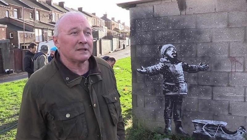 Họa sỹ Banksy bên một tác phẩm ông vẽ trên tường nhà ngoài phố