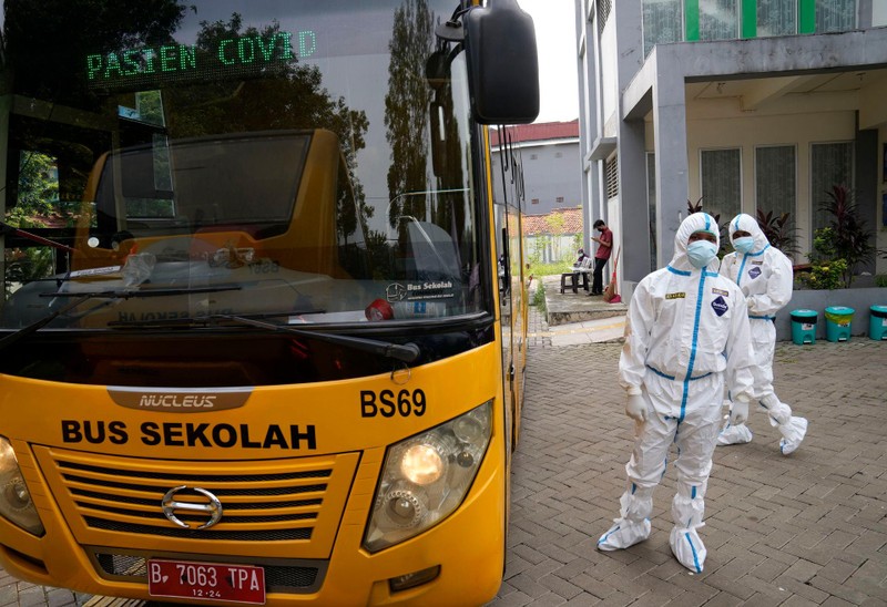 Ngày 18/6, tại một trung tâm y tế cộng đồng ở Jakarta, Indonesia, các công nhân mặc quần áo bảo hộ đang ở gần xe buýt của trường học, chuẩn bị đưa những người có kết quả xét nghiệm dương SARS-CoV-2 đến bệnh viện chuyển tuyến. (AP)