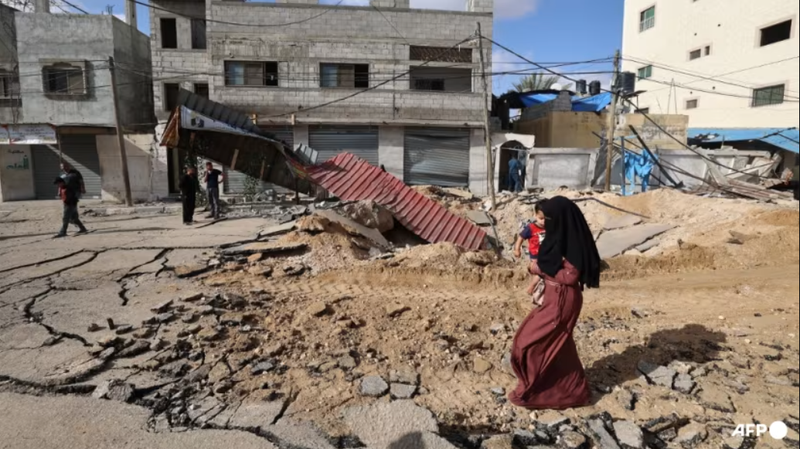 Một người phụ nữ đi bộ qua một con đường bị phá hủy sau cuộc không kích của Israel tại Khan Younis ở phía nam Dải Gaza vào ngày 14/5. Ảnh: AFP.