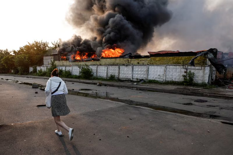 Một người qua đường đi bộ gần một tòa nhà đang bốc cháy tại địa điểm xảy ra cuộc tấn công bằng máy bay không người lái của Nga nhằm vào Kiev hôm 10/6. Ảnh: Reuters.