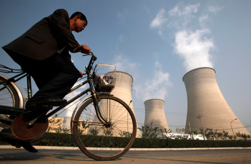 Một người đàn ông đạp xe qua ống khói của một nhà máy điện nằm ở ngoại ô Bắc Kinh vào ngày 29/10/2009. Ảnh: Reuters.