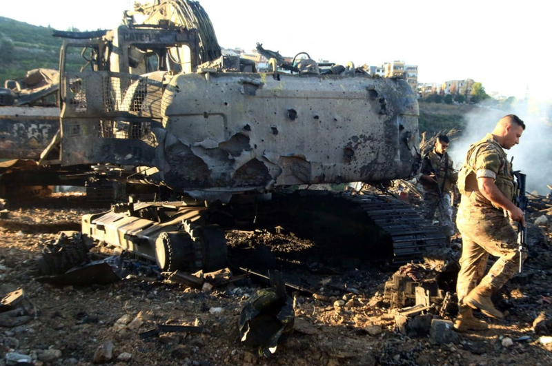Binh sĩ Lebanon đi cạnh một máy đào bị phá hủy sau cuộc không kích của Israel. Ảnh: AFP.