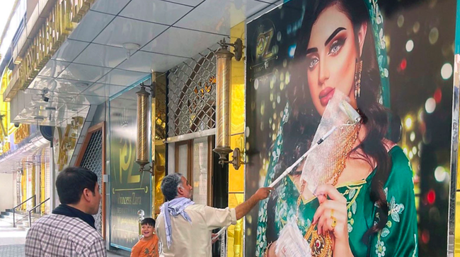 Một công nhân đang sử dụng sơn trắng để che hình ảnh quảng cáo váy cưới trước một cửa tiệm, theo chỉ thị của Taliban Một công nhân đang sử dụng sơn trắng để che hình ảnh quảng cáo váy cưới trước một cửa tiệm, theo chỉ thị của Taliban