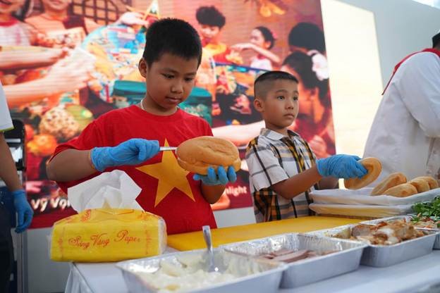 Các em bé khéo léo thêm pate và thịt quay vào ổ bánh. (Ảnh: VNA)