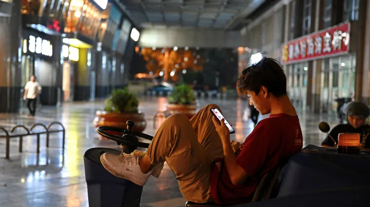 Một người đàn ông xem điện thoại bên trong một trung tâm mua sắm vắng vẻ tại Bắc Kinh, ngày 15/8 (Ảnh: CNBC) 1.png