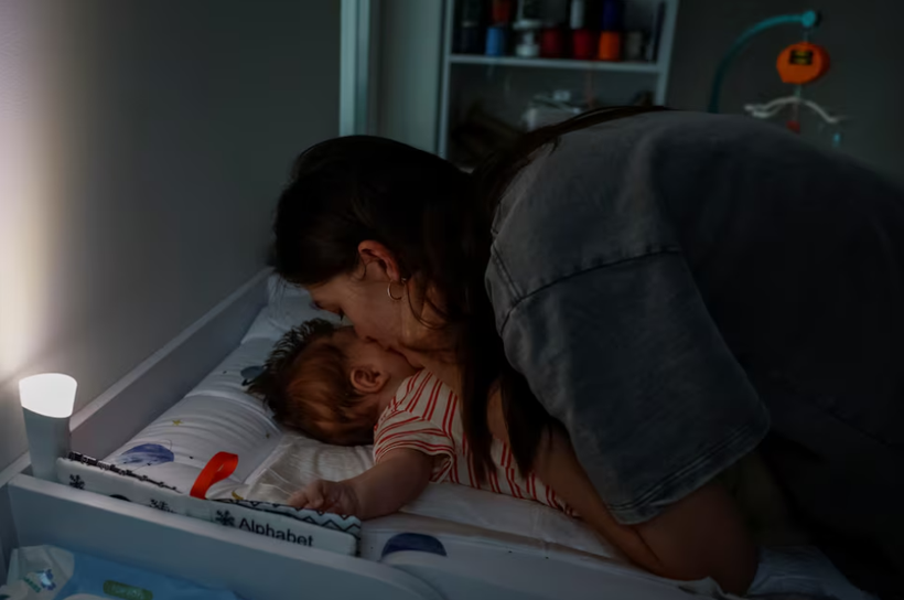 Maryna Tkalich, 33 tuổi, hôn đứa con 2 tháng tuổi của mình sau khi thay quần áo, trong lúc mất điện, ngày 7/6 (Ảnh: Reuters) 4.png